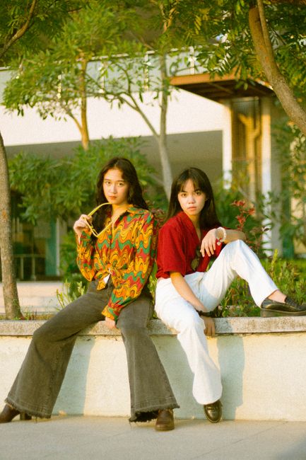 Fotomural Chicas adolescentes con estilo sentadas en un banco, vistiendo atuendos vibrantes.