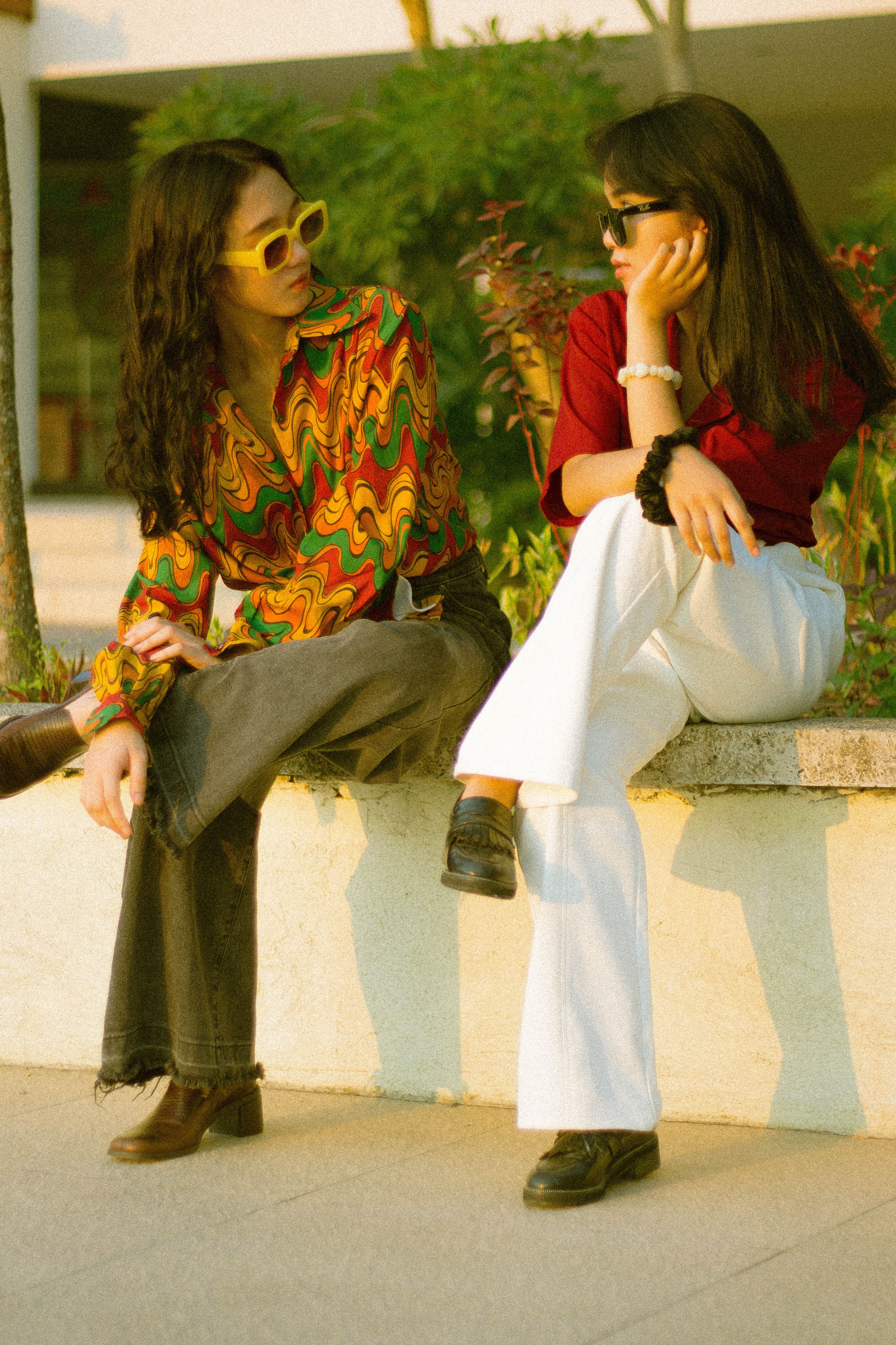 Fotomural Dos adolescentes con atuendos retro coloridos posan en un banco al aire libre, mostrando un estilo vintage.