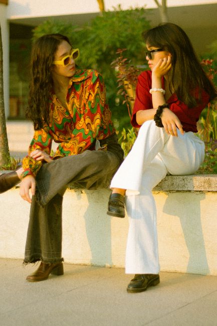 Fotomural Dos adolescentes con atuendos retro coloridos posan en un banco al aire libre, mostrando un estilo vintage.