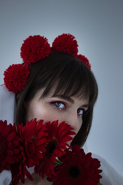 Young Woman Posing with a Red Flower Crown and Holding Red Flowers in front of Her Face