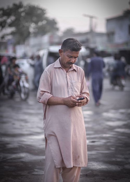 Free An adult man in traditional attire using a smartphone outdoors, capturing urban life. Stock Photo