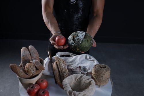 Free A man displays artisanal bread and a red apple with rustic food items on a table. Stock Photo