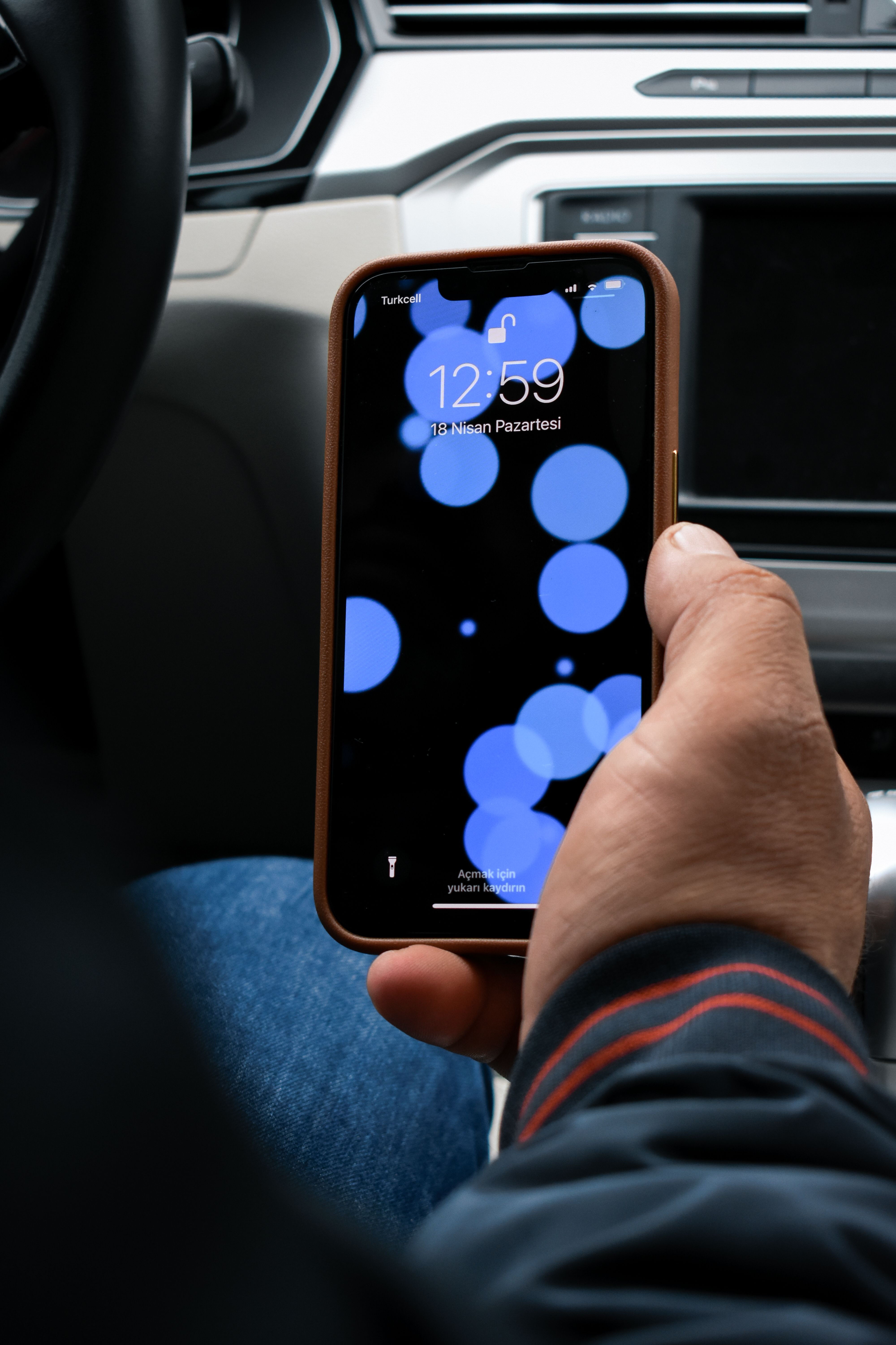 Close-up of a person holding a smartphone with an abstract, blue-themed screen in a car setting.