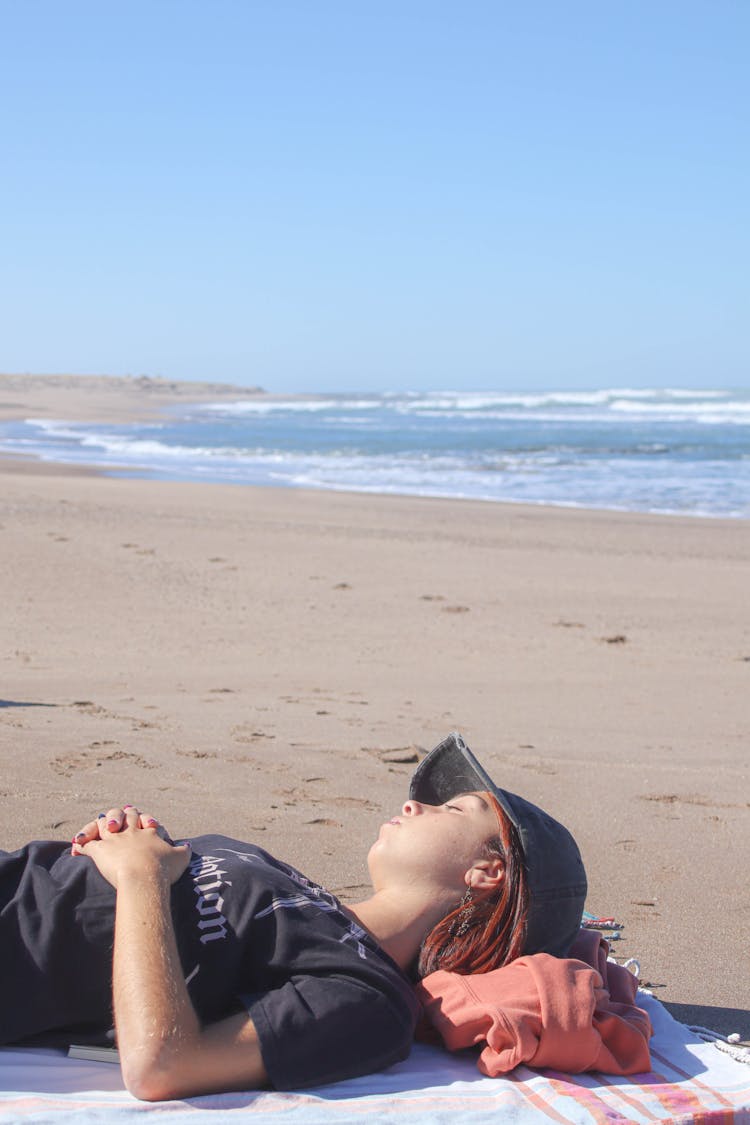 Woman In Black Shirt Wearing Hat Sleeping On Sand Near Beach 