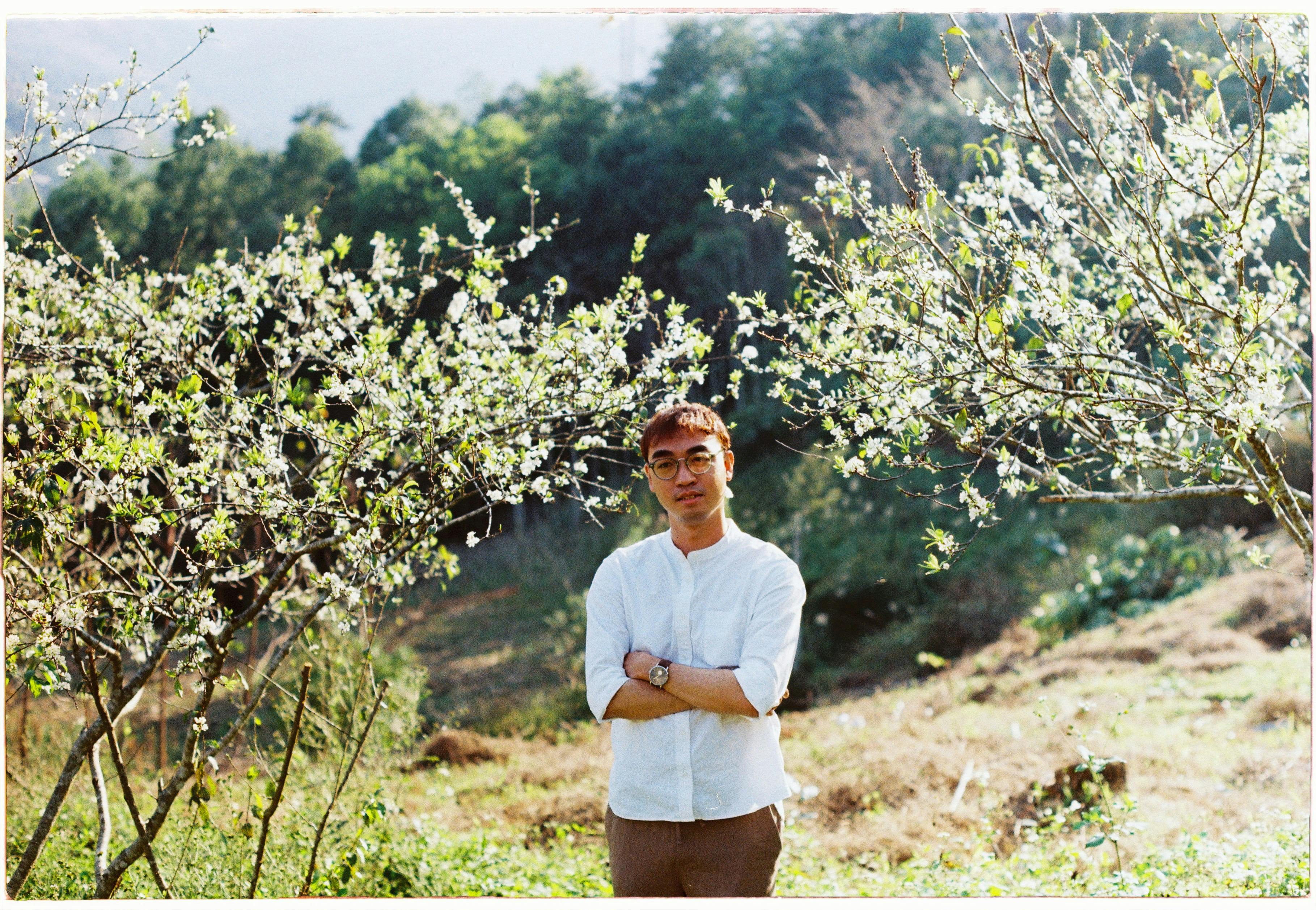 Portrait of a young man standing among flowering trees in a rural setting.