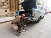 Hispanic mechanic working on a vintage car on an urban street in Cuba.