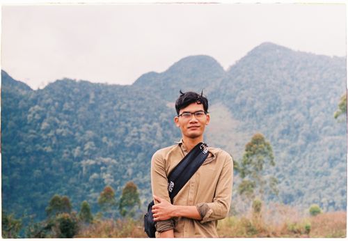 Free A smiling man with eyeglasses poses in front of lush, forested mountains. Stock Photo