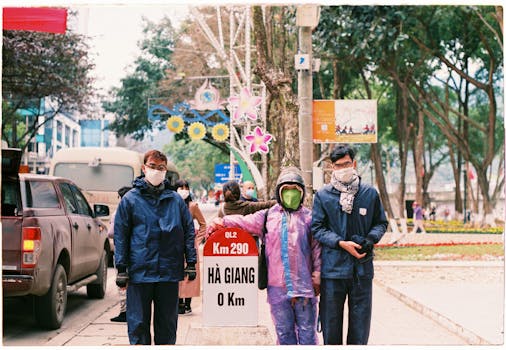 People in face masks pose by Hà Giang kilometer marker, displaying safety during pandemic.