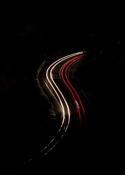 Aerial view of car light trails on a curved road at night, creating a dynamic pattern.