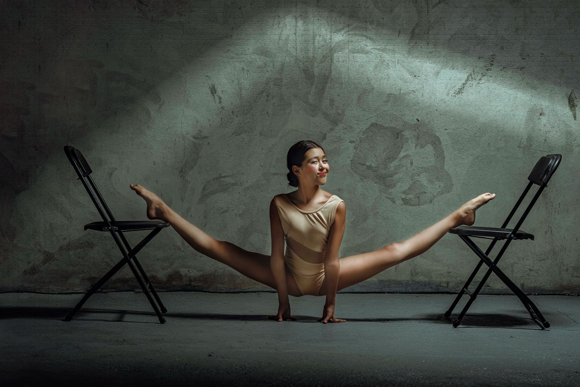 A young ballerina performing a split between two chairs demonstrating her impressive flexibility and strength.