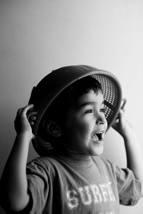 Grayscale Photo of a Boy with Strainer on Head