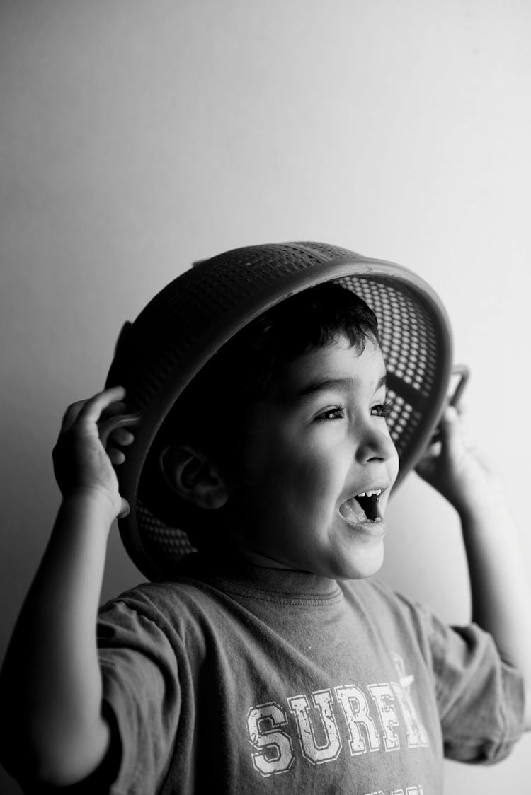 Grayscale Photo Of A Boy With Strainer On Head