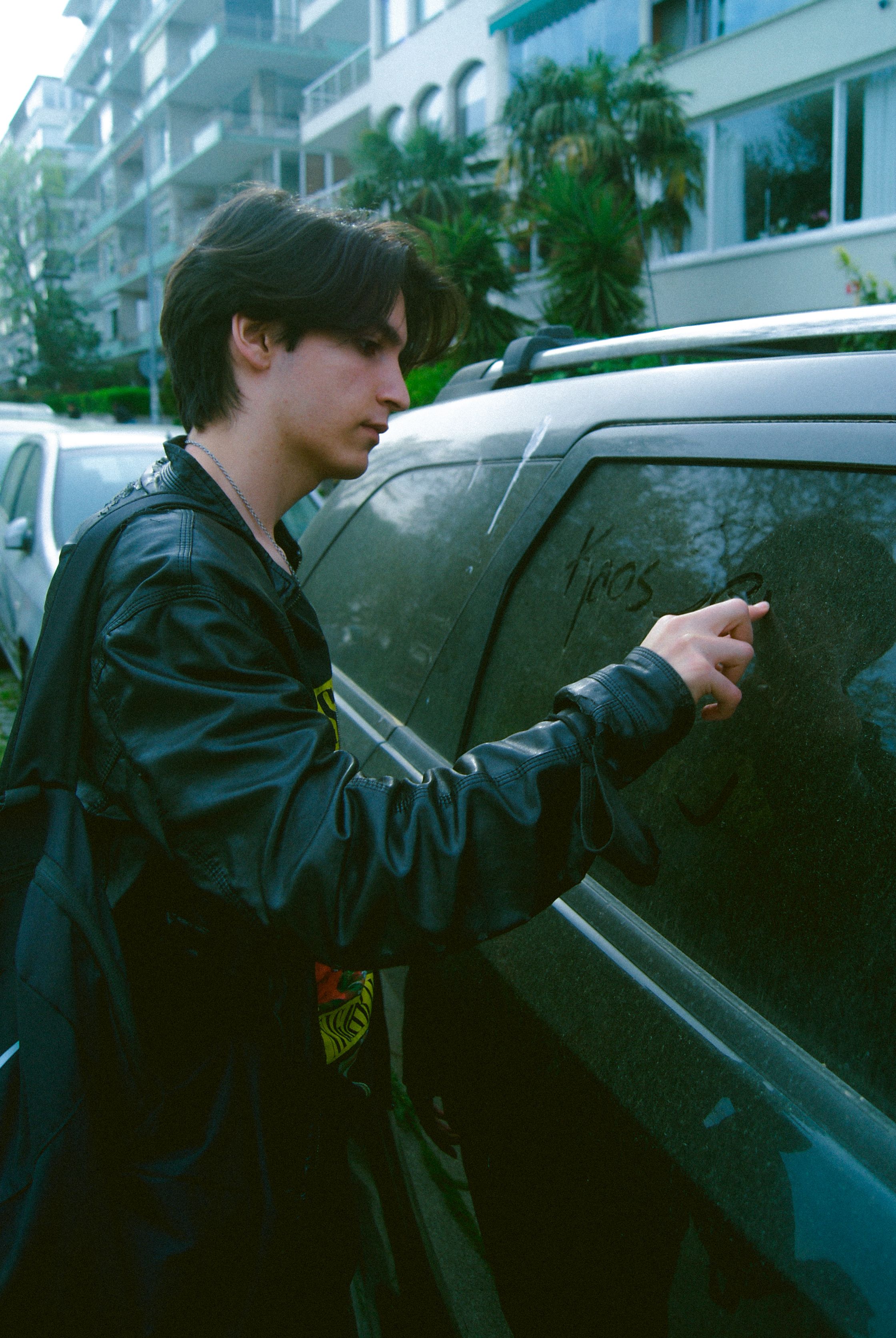 Teenager writes on a dusty car window in an Istanbul street, capturing youth culture.