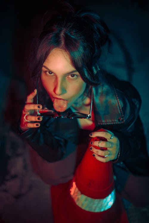 Woman in Black Leather Jacket Sitting Beside Traffic Cone