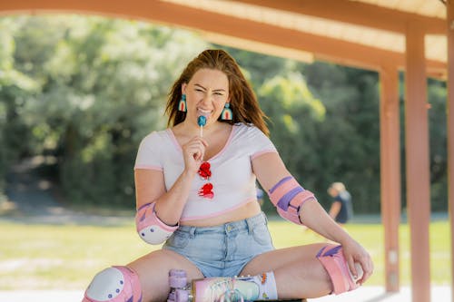 A Woman with Elbows and Knee Pads Eating Lollipop