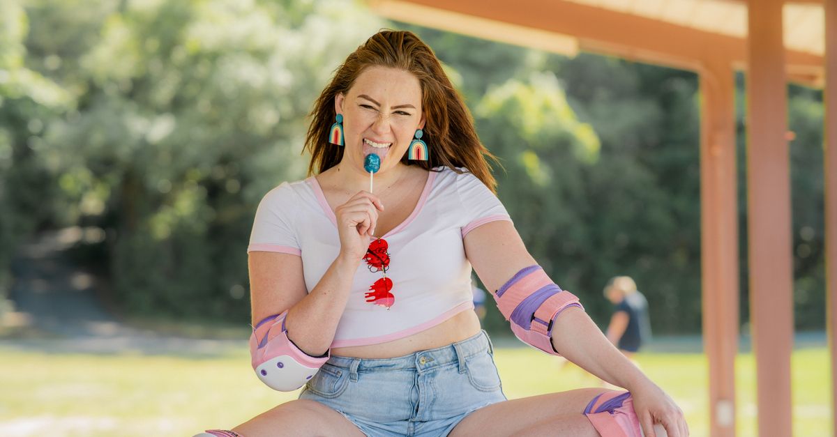Cheerful woman with roller skating gear enjoying a lollipop in a sunny park.