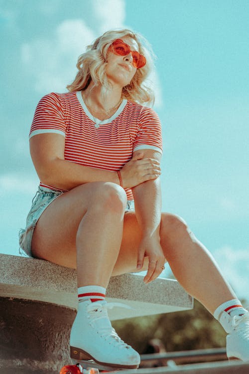 Woman in Red and White Striped Shirt and Blue Denim Shorts Wearing Roller Skates Sitting on Bench 