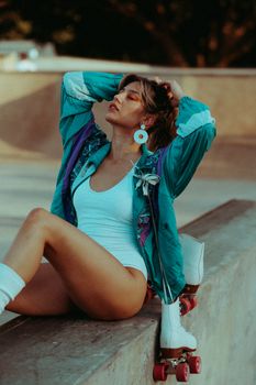 Fashionable woman posing with roller skates at an outdoor skate park in a colorful jacket.