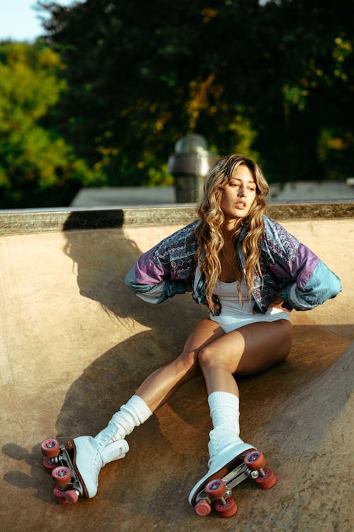 Woman Wearing a Colorful Jacket over a White Bodysuit Sitting on a Skate Ramp