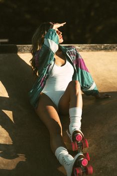 Woman in a bodysuit and jacket roller skating, enjoying the sun in an urban environment.