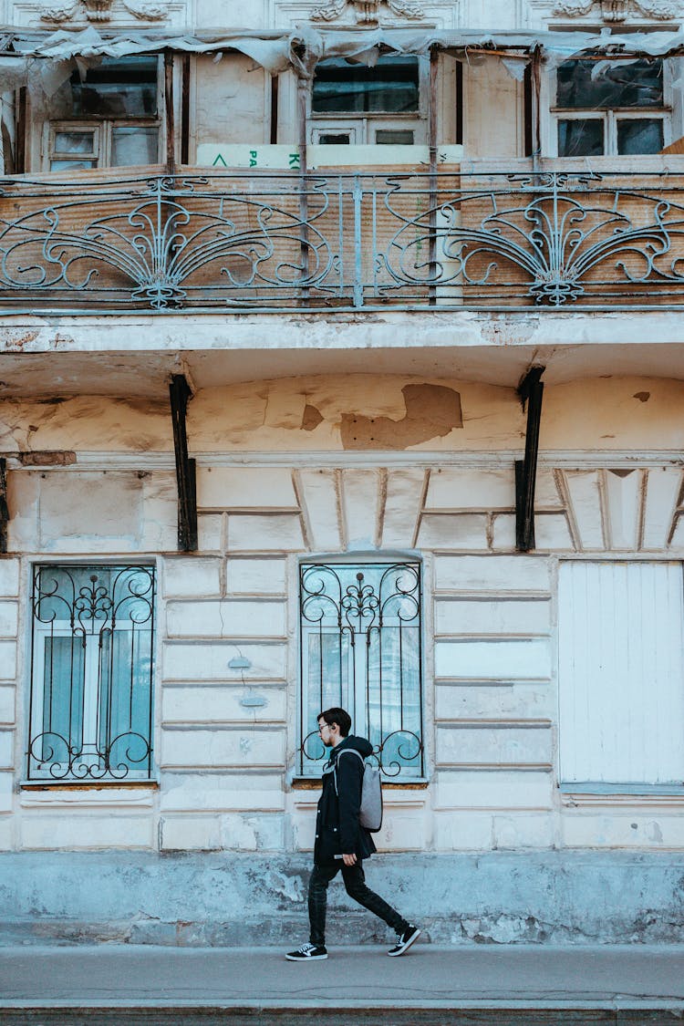 A Man In Black Jacket Walking Beside An Old Building