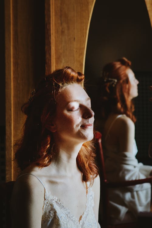 Free Redhead Woman with Closed Eyes Sitting by Mirror Stock Photo