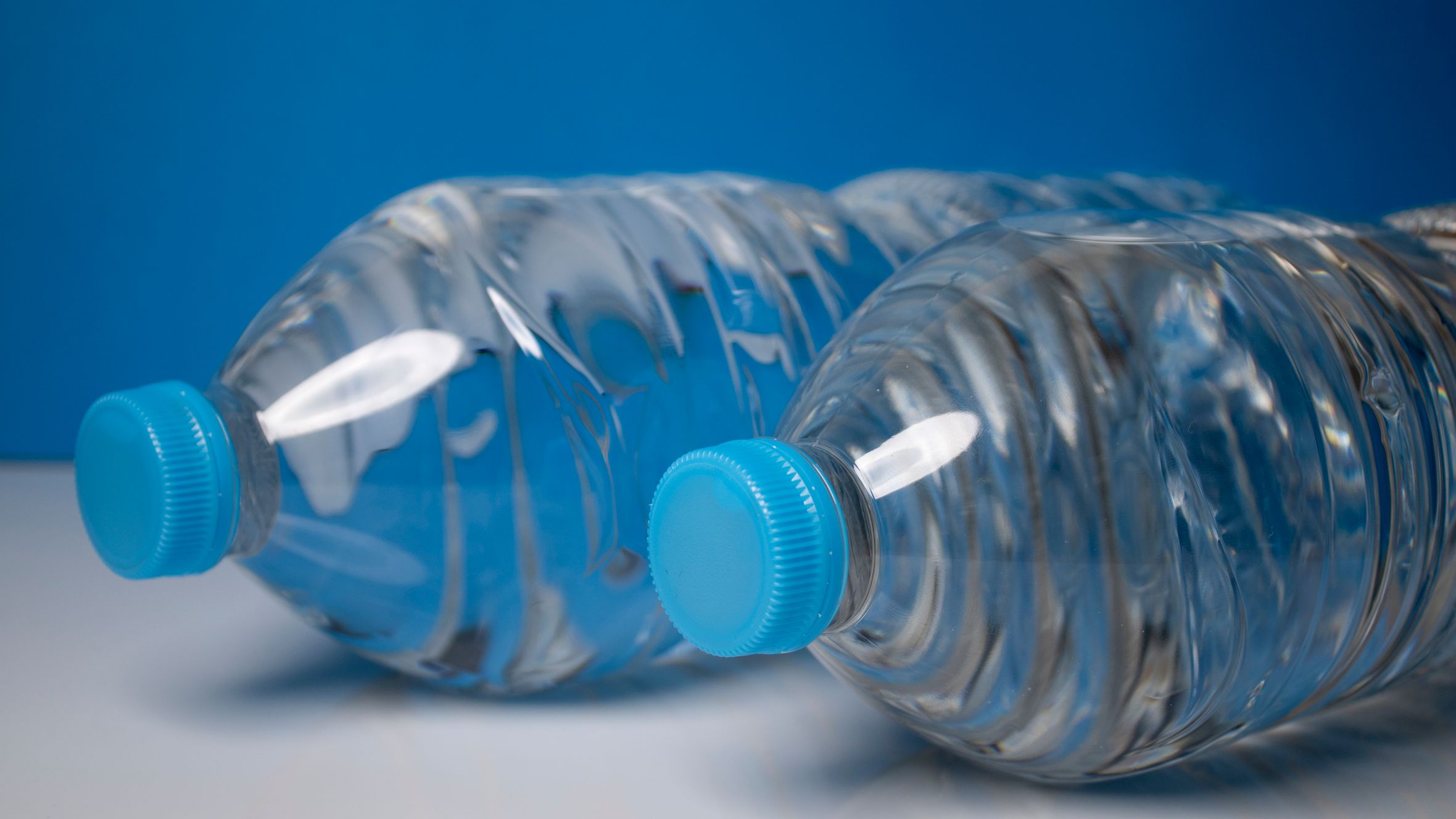 Close-up of clear plastic water bottles with blue caps on a blue background.