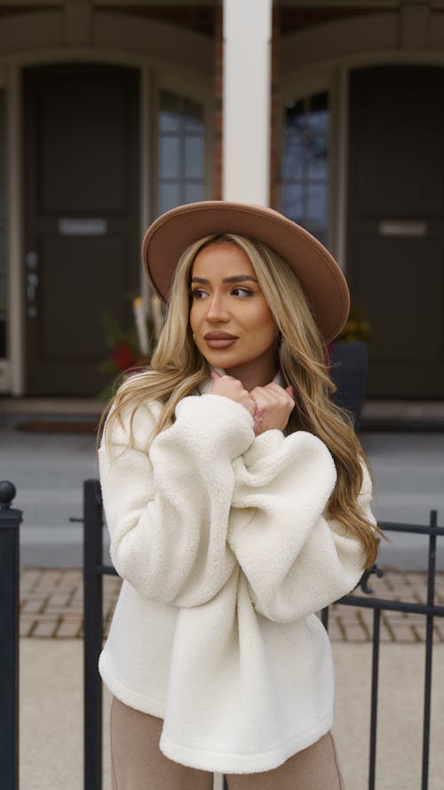 Young Woman Wearing a Sweater and a Hat Posing on a Sidewalk in City 