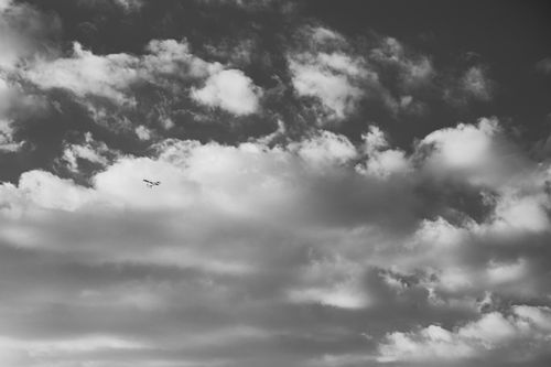 Free A black and white photo of clouds with a small aircraft flying above. Stock Photo