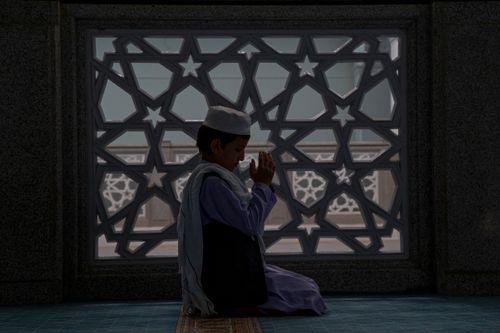 Free Boy kneeling in prayer inside mosque, reflecting Islamic faith and tradition. Stock Photo