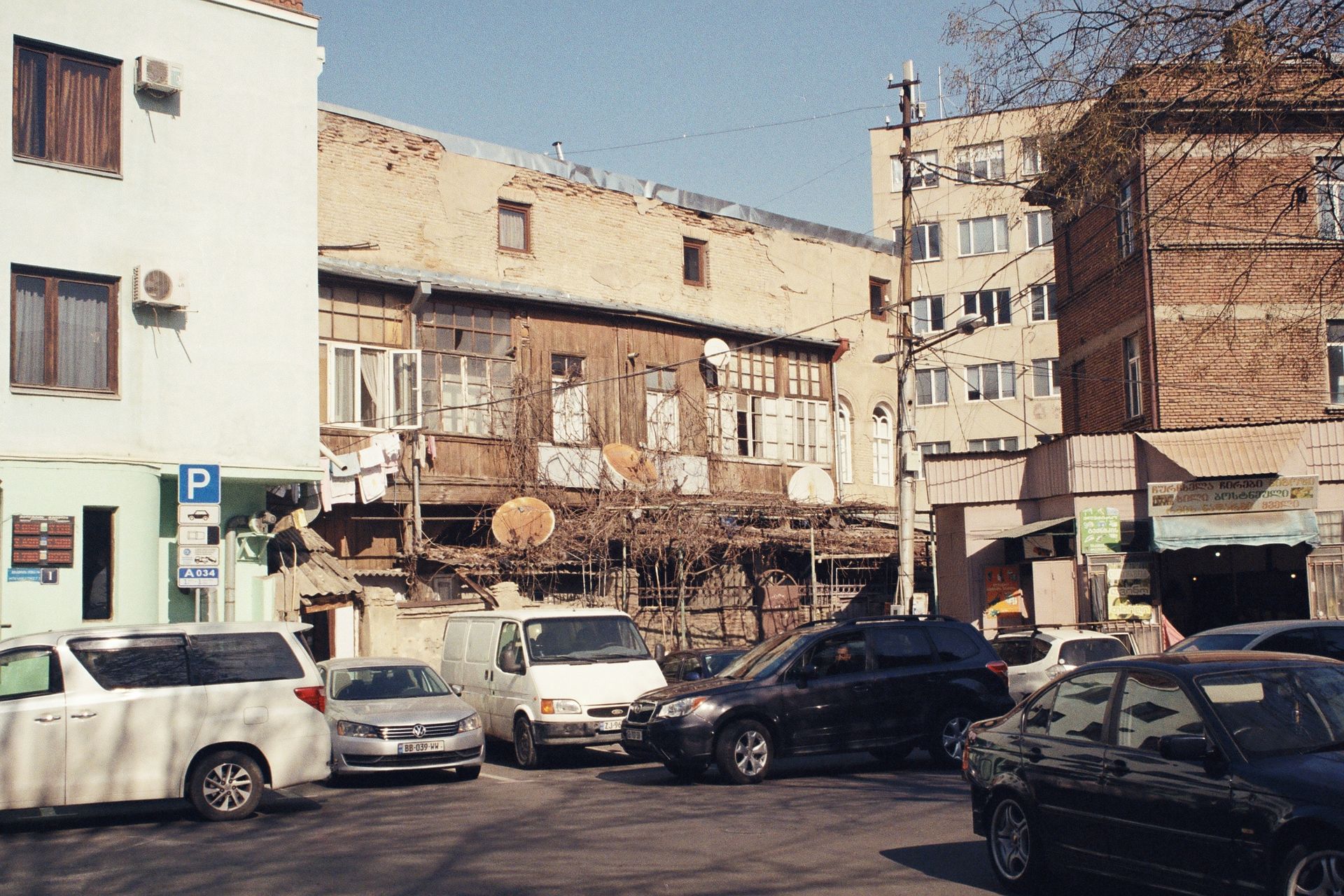 Busy urban street with residential buildings, parked cars, and satellite dishes in view.