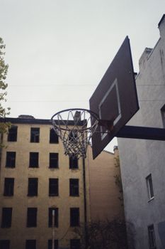 A basketball hoop in an urban setting surrounded by old, abandoned buildings.