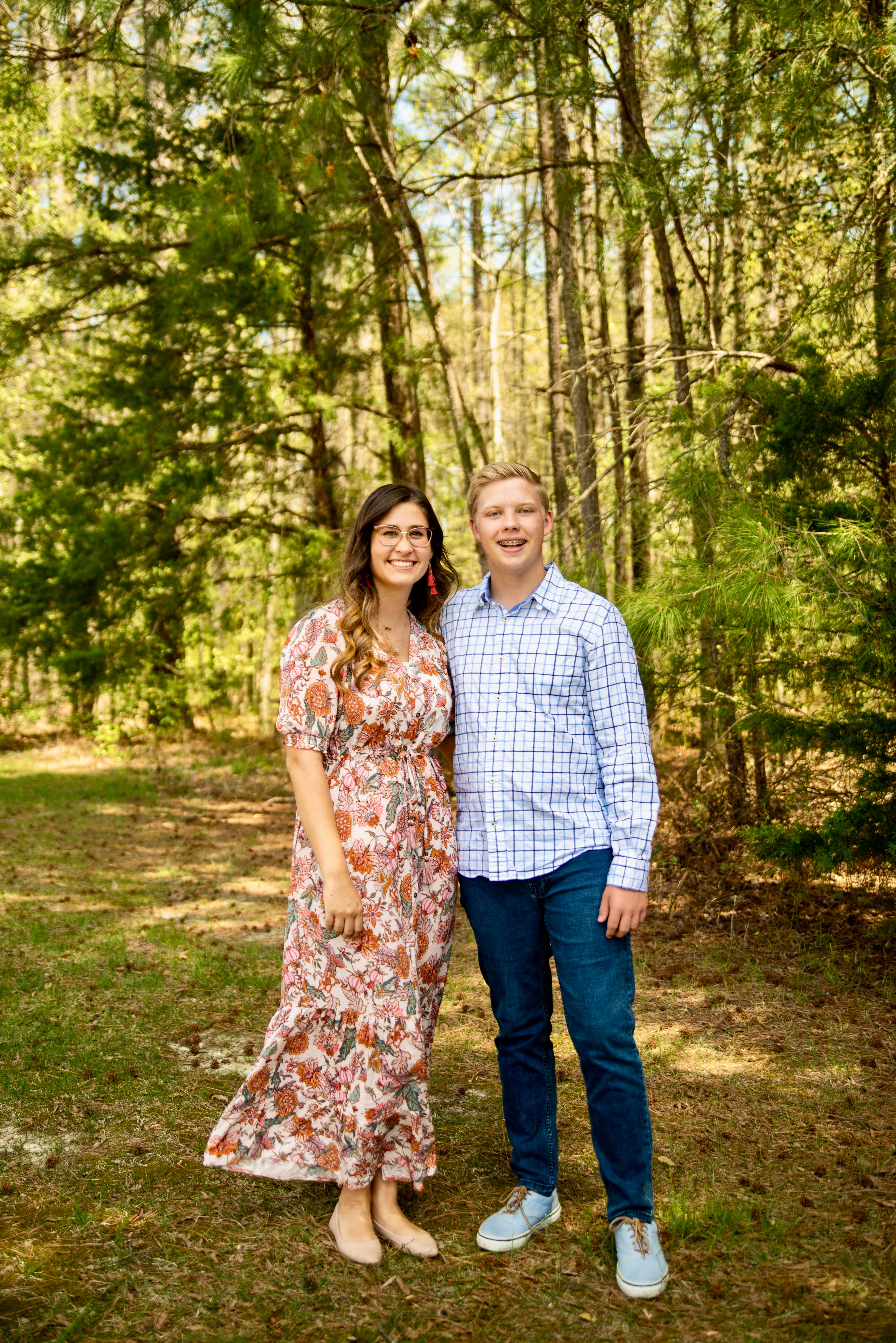 A happy couple poses together in a sunlit forest, capturing a moment of love and nature.