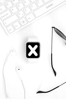 Overhead shot of a smartwatch, keyboard, earbuds, and sunglasses on a white background.