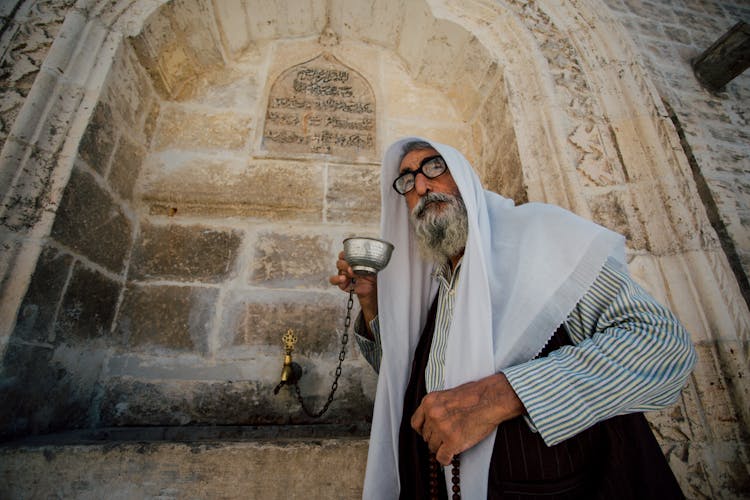 Man In Headscarf Drinking From Public Fountain