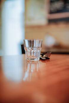 Simple and elegant glass cup on a reflective wooden table with blurred background.