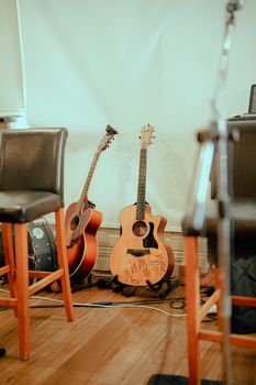Two acoustic guitars resting indoors, surrounded by chairs, with a warm and inviting ambiance.