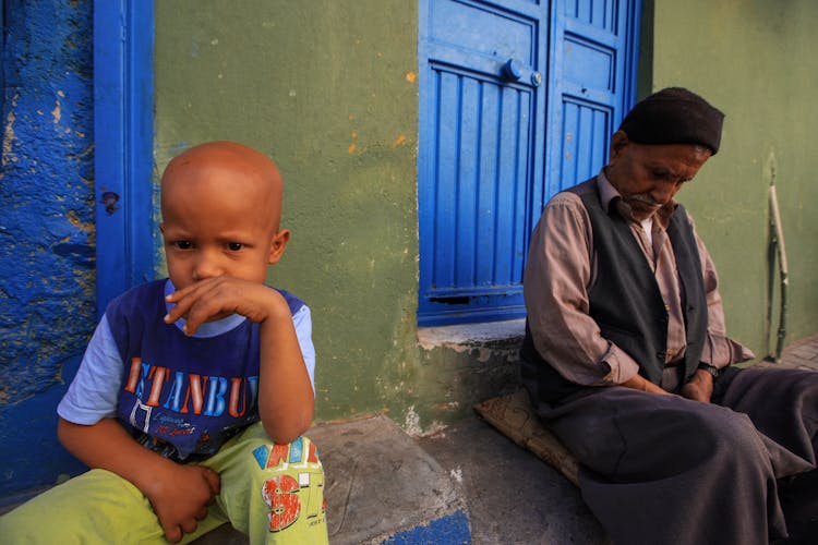 Bald Boy Sitting Near Sleeping Man