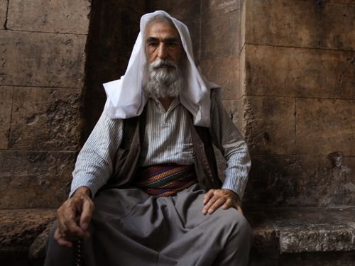 Free Portrait of a senior man with a beard and mustache in traditional clothing, sitting indoors. Stock Photo