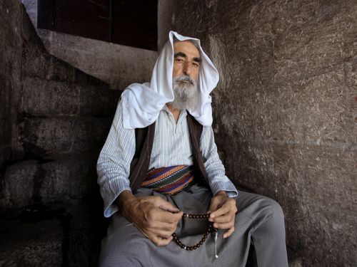 Free Portrait of an elderly man sitting indoors, holding prayer beads, showcasing spirituality and tradition. Stock Photo