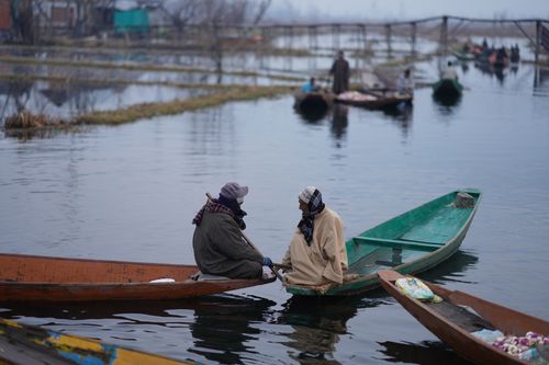Free Two individuals engage in conversation in wooden boats on a serene lake with scenic surroundings. Stock Photo