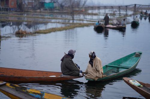 Free Two fishermen engage in conversation on their boats in a serene river setting, dressed warmly for the weather. Stock Photo