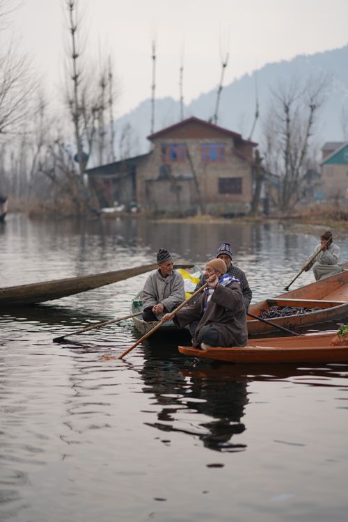 Free Men paddling traditional wooden boats on a calm lake in urban setting. Stock Photo