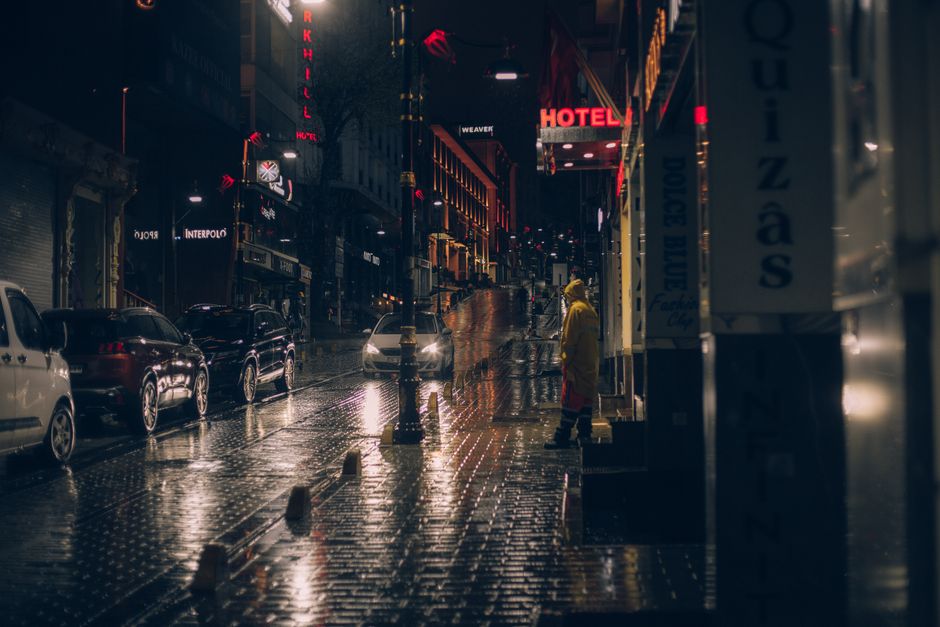 Moody rainy night scene with city lights, wet streets, and a solitary figure.