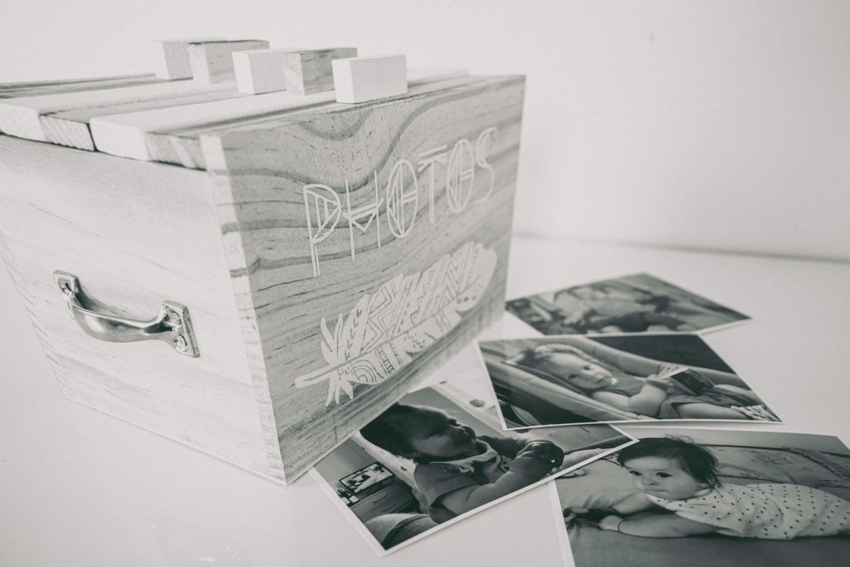 A wooden photo box labelled Photos with black and white baby photographs scattered on a white surface