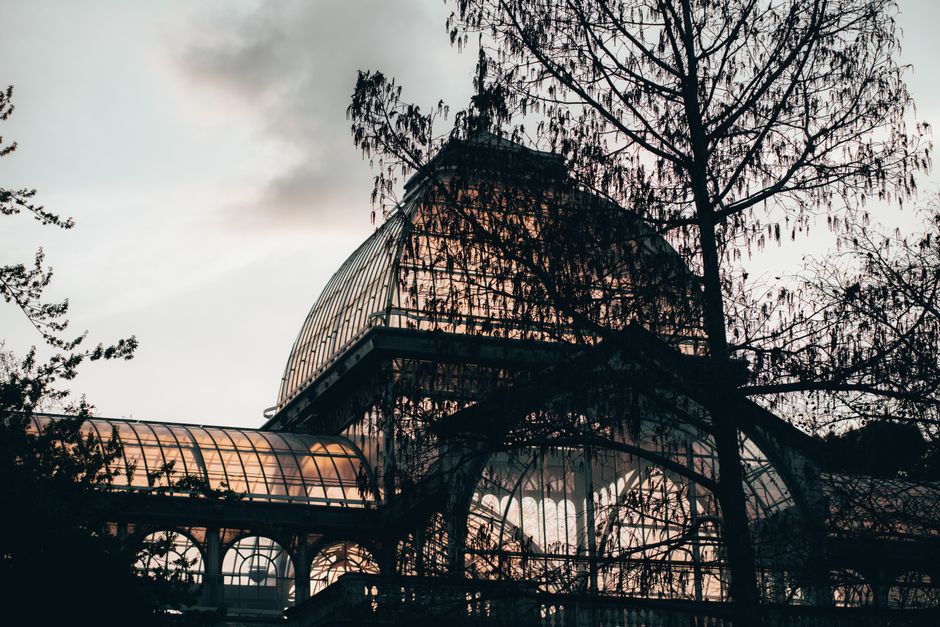 The iconic glass structure of Palacio de Cristal contrasts against a dusky sky in Madrid, Spain.