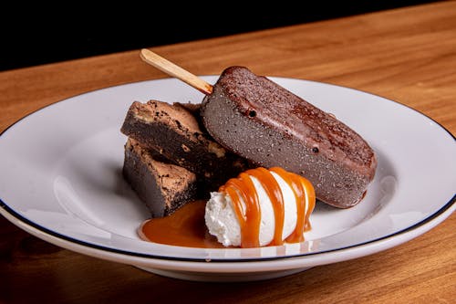 Delicious Brownies and Chocolate Ice Cream on Stick Beside Cream on White Plate