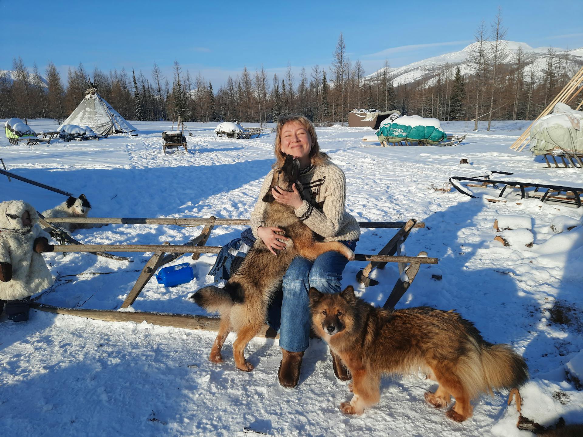 A Woman in Brown Sweater Sitting on Sled Hugging a Brown Dog