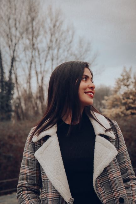 A woman in a checkered coat smiles outdoors on a brisk winter day.