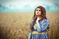 一位身着蓝色传统服装的美丽女子，优雅地站在田野中，拥抱自然